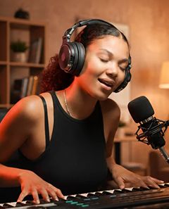 A singer wearing headphones at a microphone and keyboard during an online music session