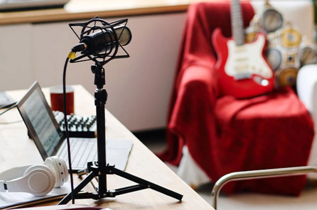 Microphone and laptop on a desk with a guitar in the background for virtual vocal classes  