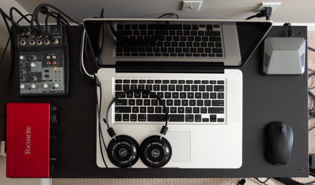 Computer desk with headphones, mixer, and laptop ready for online singing lessons