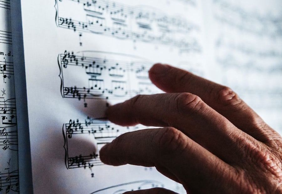 A hand resting on an open page of piano sheet music, reaching toward the next line of the grand staff