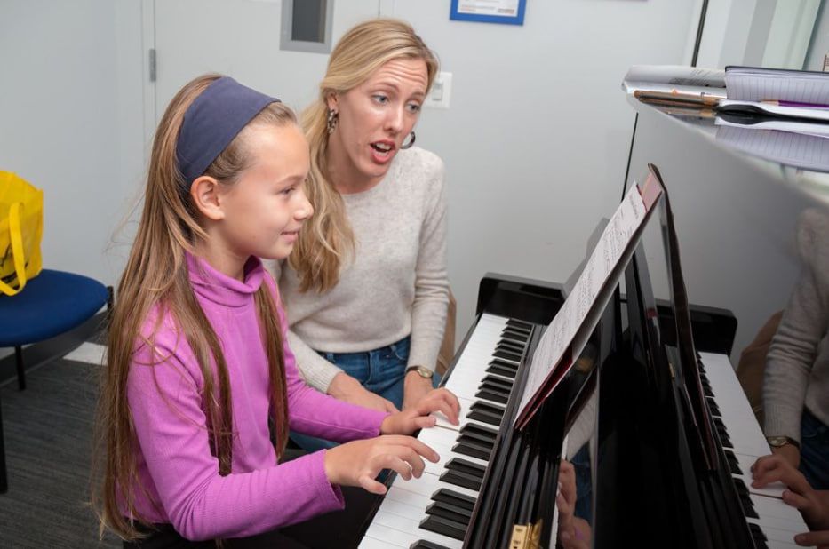professional piano teacher guiding young student during in-person lesson
