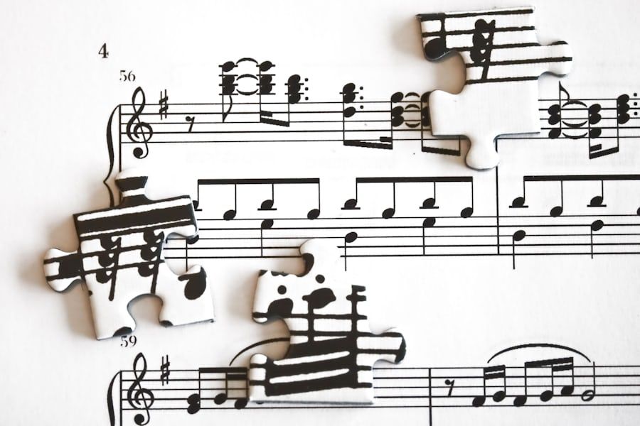 A page of printed sheet music with jigsaw puzzle pieces cut from music notation lying on top of it