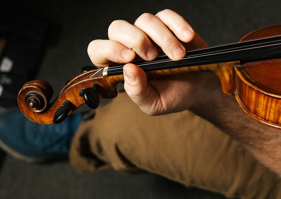 Close-up of a violinist's left hand on the neck, fingers curved over the strings from above and the thumb resting on the side of the neck