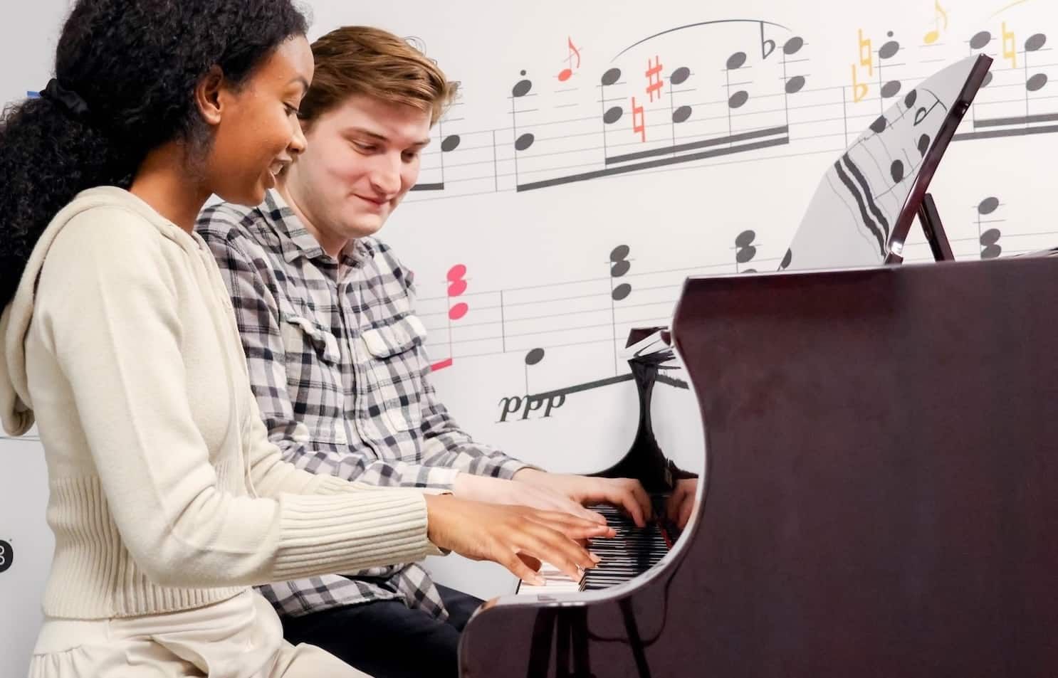 Experienced piano teacher guiding a smiling adult student at the keys in a bright NYC studio