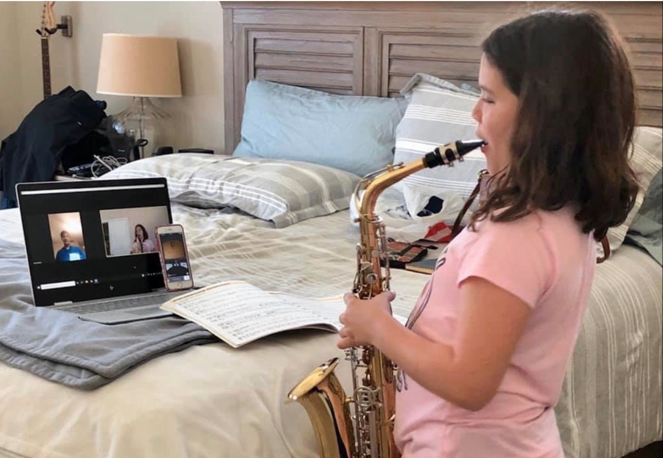 Young girl playing saxophone while taking an online music lesson on laptop